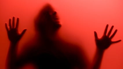 A man screams in anguish behind translucent red glass.